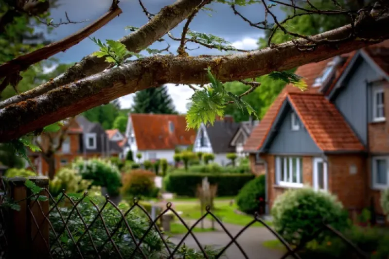 Gartenlandschaft in einer Villengegend, im Vordergrund ein Bau, dessen Äste über den Zaun ragen