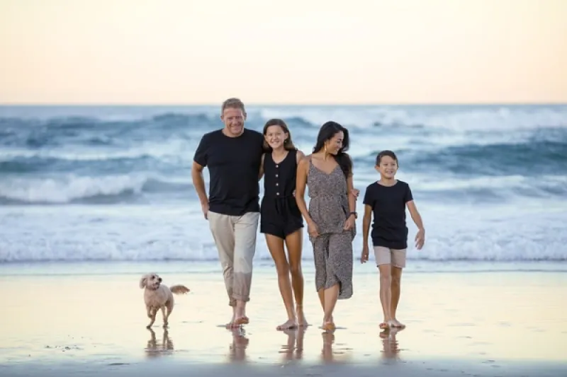 Familie mit Vater, Mutter und zwei Kindern spazieren an einem Strand