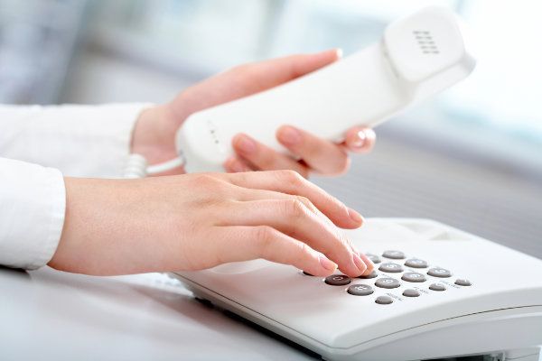 HĂ€nde einer Person, die ein weiĂes Telefon mit Tasten bedient